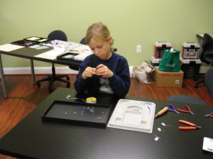 A young girl works on beading a necklace at a class offered by The Twisted Bead & Rock Shop.